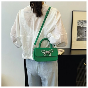 Detail of green crossbody bag with a large silver rhinestone bow on the flap cover