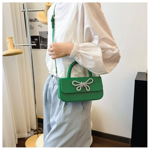 Close-up of bright green handbag featuring a silver rhinestone bow and leather top handle