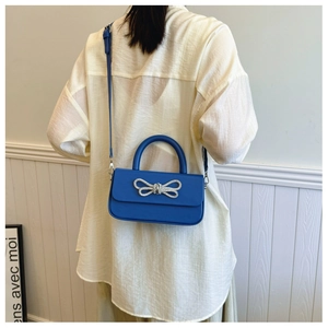 Detail of Klein blue crossbody bag with rhinestone bow on white shirt outfit