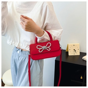 Detail of red crossbody box bag featuring a sparkling silver rhinestone bow decoration