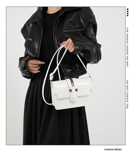 Bolso bandolera de cuero blanco con hebilla dorada sobre una chaqueta de cuero negro