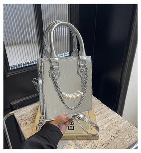 Detail einer silbernen Faltenhandtasche mit weißen Perlen und dekorativen Metallkettengliedern
