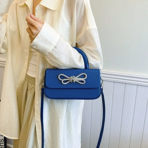 Blue crossbody box bag with rhinestone bow and leather handle shown on model