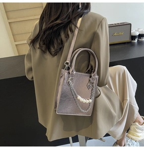Detail einer silbernen Metallic-Handtasche mit Perlenkette und Kunstleder-Textur