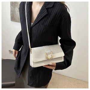 Détail de la texture crocodile blanc crème et boucle fer à cheval dorée sur le sac