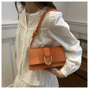 Détail d'un sac à bandoulière orange vif avec texture crocodile et boucle dorée en U