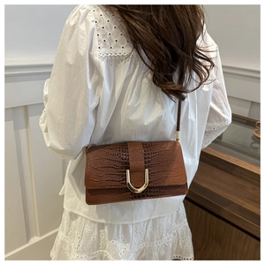 Détail d'un sac bandoulière marron motif crocodile avec boucle fer à cheval dorée sur dentelle