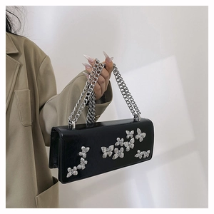 Close-up of black glossy leather bag with silver butterfly charms and chunky chain