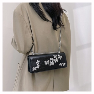 Detail of a black crossbody chain bag with silver butterfly charms worn on a blazer