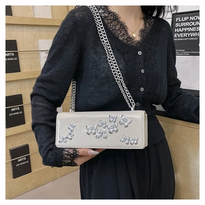 Detail of silver 3D butterfly patches and metallic chain on cream-colored handbag