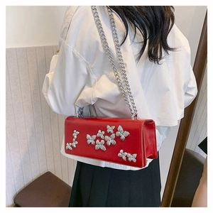 Detail of red butterfly crossbody bag with silver chain strap worn by a model