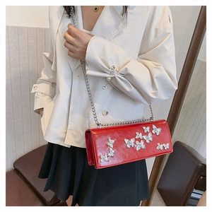 Close-up of red patent leather crossbody bag with silver butterfly charms and chain strap