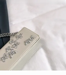 Close-up of silver butterfly ornaments and metal chain on beige leather square bag