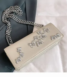 Detail of cream flap bag featuring silver butterfly embossed accents and thick metal chain