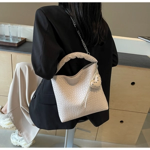 Detail der cremefarbenen Beuteltasche mit Krokodilprägung, Flechtgriff und Herzanhänger