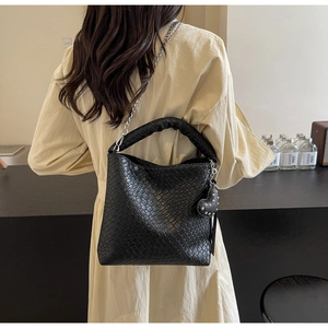 Detail einer schwarzen geflochtenen Beuteltasche mit Silberkette und Herzanhänger