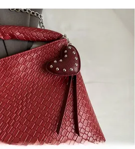 Detail der burgunderroten geflochtenen Tasche mit Herz-Charm und silberner Metallkette