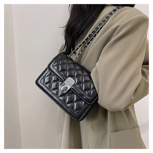Detail of black quilted crossbody bag with silver twist lock and chain strap on model