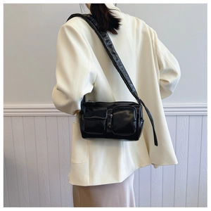 Detail of black glossy multi-pocket crescent bag with pleated texture and wide strap