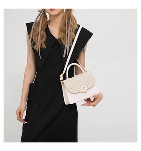 Detailed view of a cream white woven crossbody bag with gold buckle on a black dress