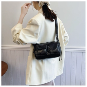 Detail of black glossy crescent bag with utility pockets worn over a beige blazer