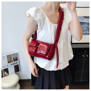 Close-up of a glossy red PU leather crossbody bag featuring functional 3D pockets and wide strap