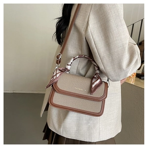 Chic small square bag with silk scarf handle detail worn by a model in a casual setting