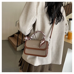 Detail of khaki textured crossbody bag with brown leather trim and silk scarf handle
