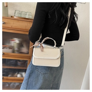 Detail of beige textured flap bag with decorative silk scarf on handle worn by model