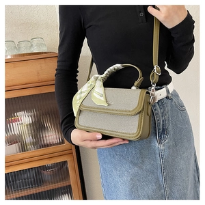 Detailed view of an olive green handbag featuring a patterned silk scarf on the top handle