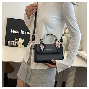 Modern black crossbody bag styled on model with decorative scarf handle and shoulder strap