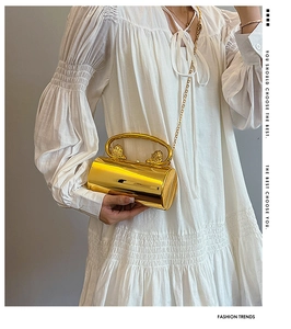 Detailed view of gold cylinder evening bag with lion head carvings and metal chain strap