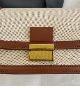 Detail of beige linen crossbody bag with brown leather trim and gold metal buckle