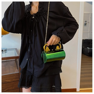 Detail of emerald green cylinder evening bag with gold lion head handle and chain strap