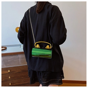 Detail of emerald green cylindrical evening bag with gold lion head handle and chain