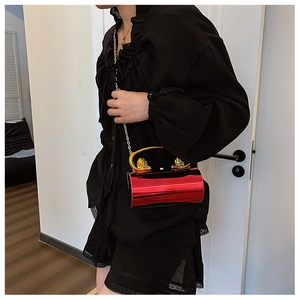 Model wearing a red hard shell cylindrical bag with a golden lion handle and chain strap