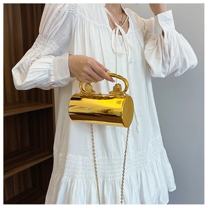 Detail of gold cylindrical clutch bag featuring dual lion head hardware on the handle