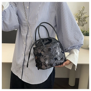 Close-up of stylish black sequin bucket bag with drawstring and silver chain strap