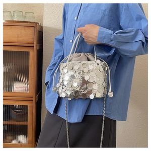Detail of a silver sequined bucket bag with a chain strap and drawstring.