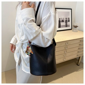 Close-up of black lychee grain bucket bag with colorful silk scarf on the handle