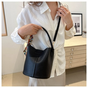 Detail of black pebbled leather bucket bag featuring a colorful silk scarf on handle