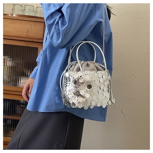 Close-up of sparkling silver sequin bucket bag with metal chain strap on shoulder