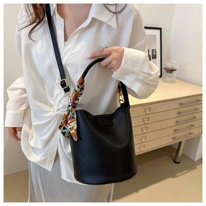 Detail of black pebbled leather bucket bag with a colorful silk scarf on the gold handle