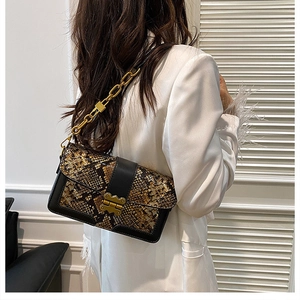 Close-up of snake skin pattern handbag with gold chain strap worn with white suit