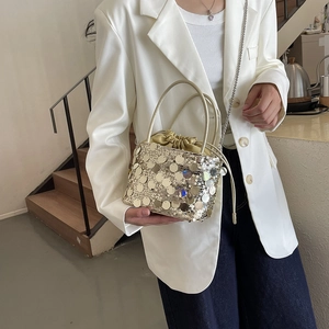 Chic gold sequin bucket bag with metal chain strap worn with white suit outfit