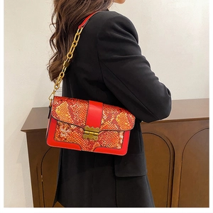 Detail of red and orange snake print handbag with golden chain strap on model