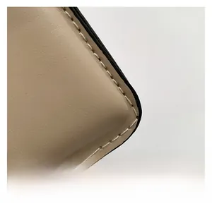 Detailed close-up of beige leather bag corner with white decorative stitching and smooth edges