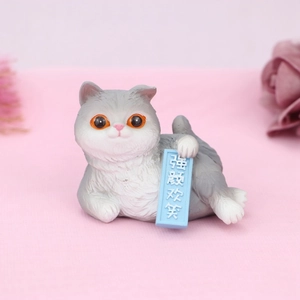Macro detail of cartoon cat resin ornament with orange eyes holding a blue sign