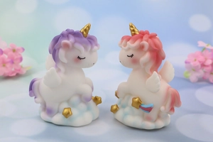Detail of cartoon unicorn figurines set on blue cloud base with gold stars and wings