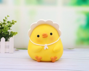 Detail of a cute yellow chick coin bank with white wavy hat on white wooden table